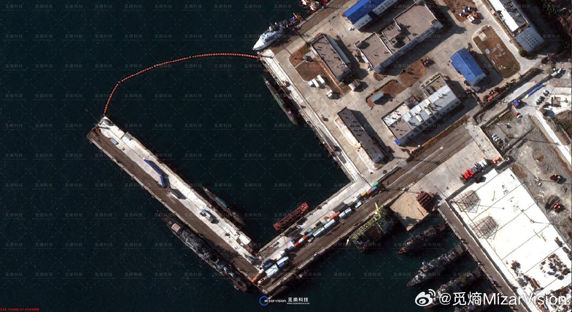 High-resolution satellite image showing the entrance to the inner harbour at Novorossiysk closed off by an arc of floating boom running from the end of the mole to the quay wall