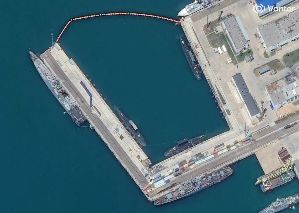 Satellite image of the inner harbour at Novorossiysk on 17 June 2026: submarines afloat alongside the quay walls, with a boom closing the harbour entrance