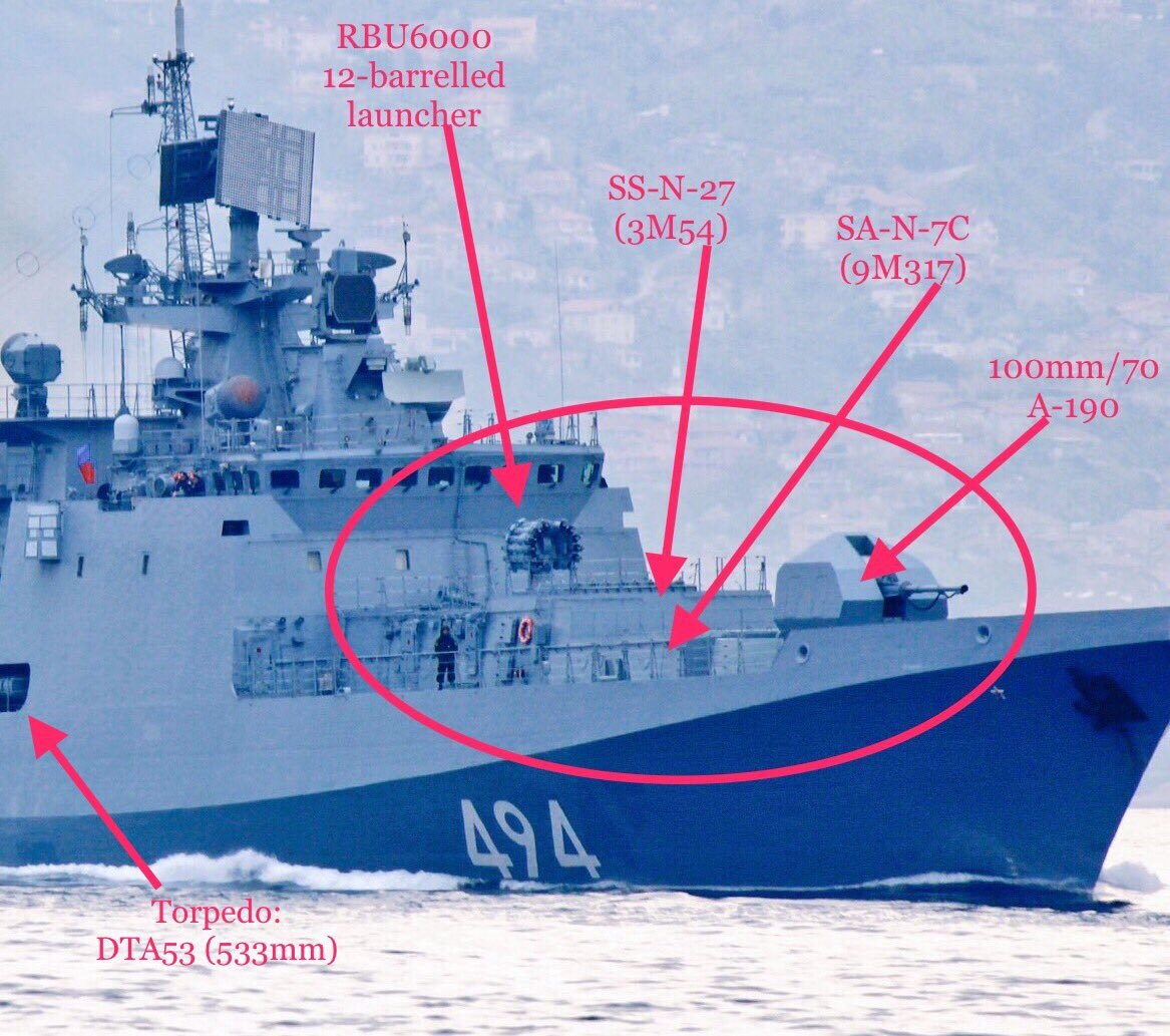 Photograph of the forward section of a Project 11356R frigate with pennant number 494 under way at sea, with arrows labelling the RBU-6000 rocket launcher, the vertical launch cells for Caliber and for the surface-to-air system, the 100 mm A-190 gun mount and the torpedo tubes